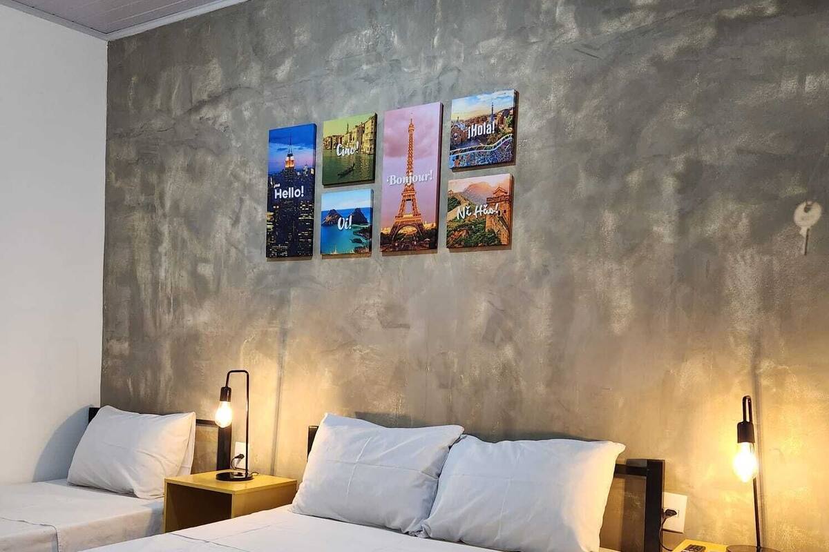 Une chambre d’hôtel avec deux lits, un mur en béton et quatre tableaux représentant des monuments célèbres.