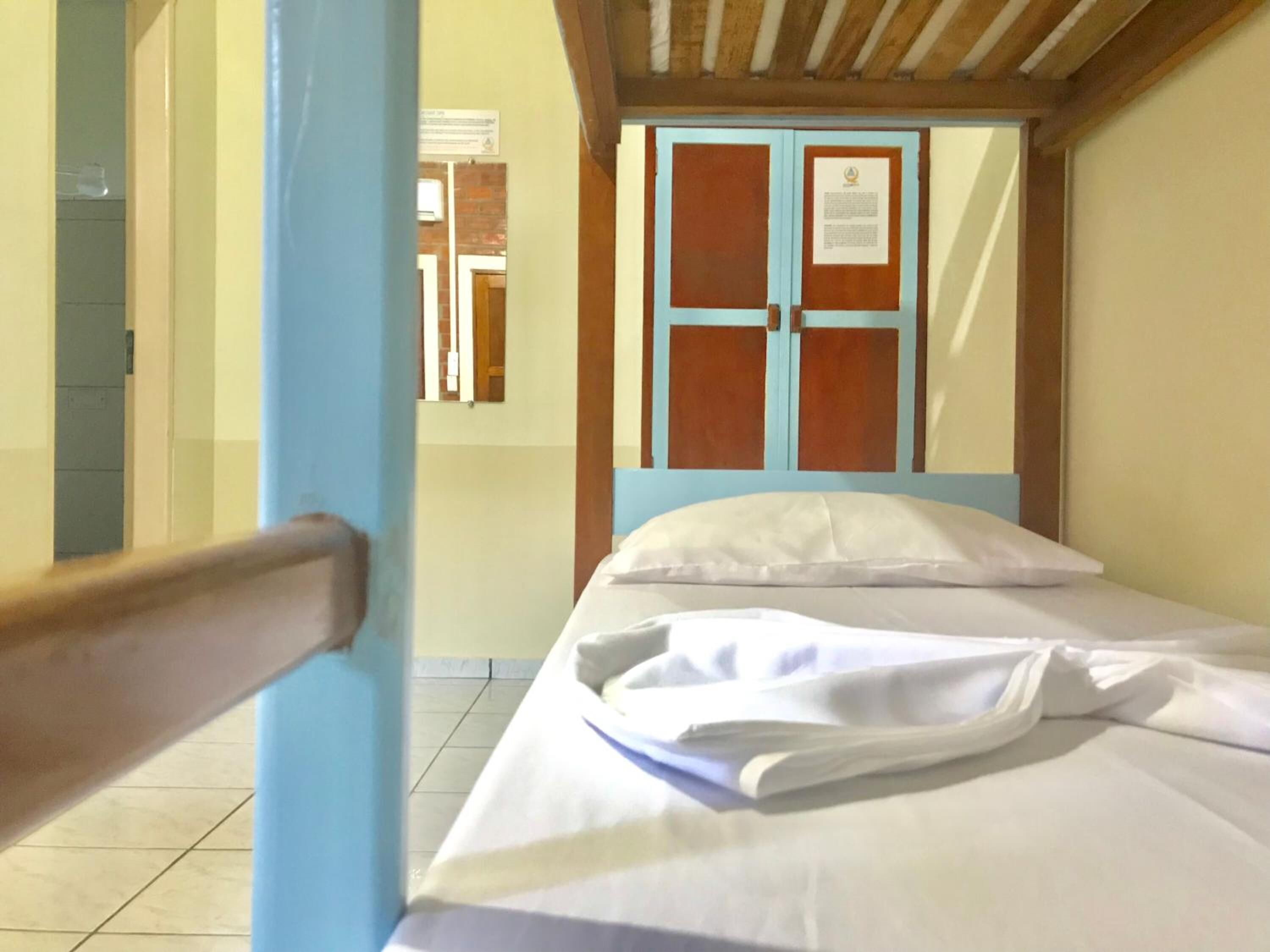 A single bed with white linens in a room with a wooden ceiling and a blue door.
