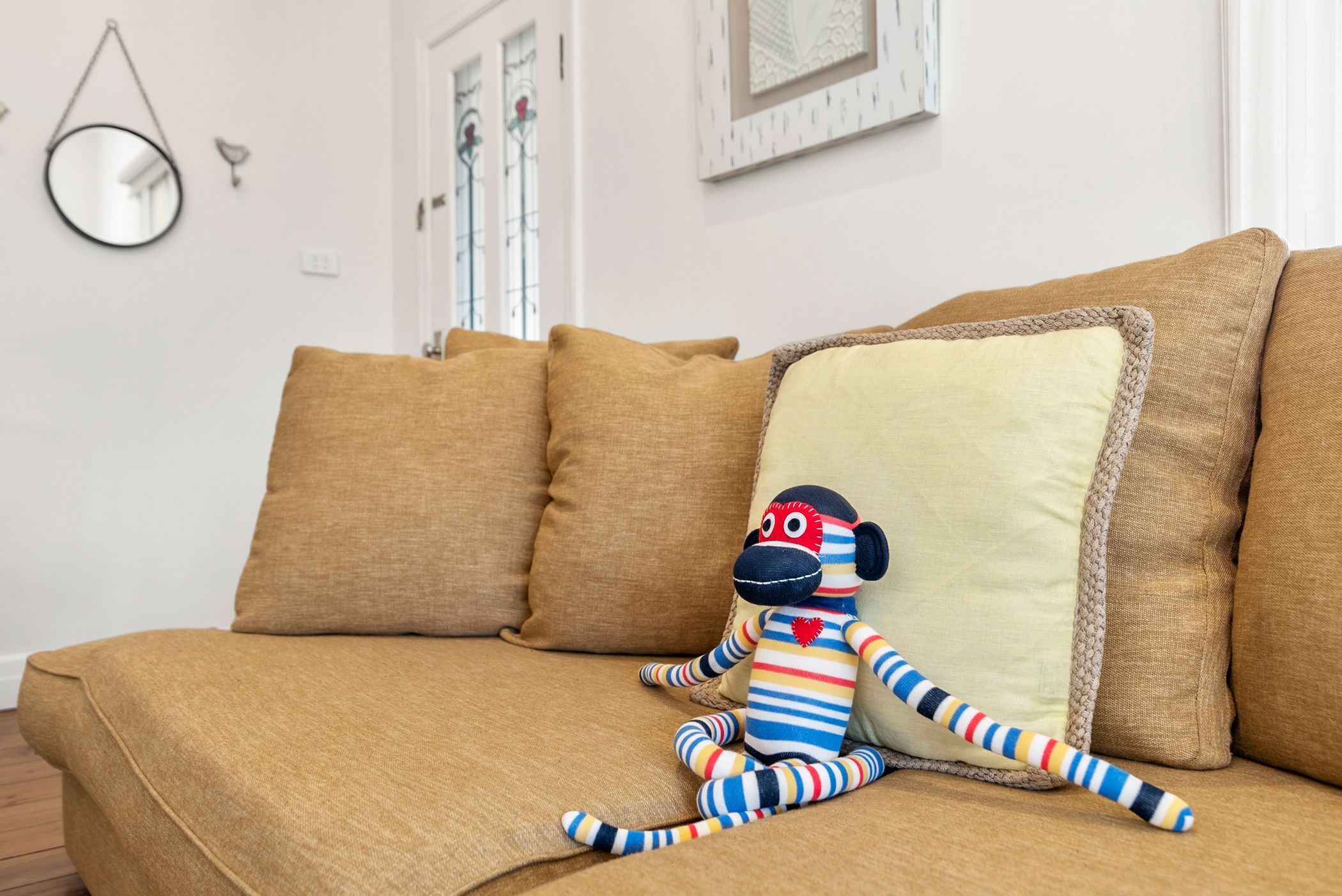 A brown sofa with a striped monkey toy and a cushion.