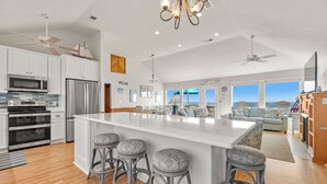 Una cocina moderna con armarios blancos, electrodomésticos de acero inoxidable, una isla grande con taburetes y vistas al área de estar.