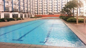 A swimming pool with clear blue water, surrounded by a tiled deck and palm trees. - Light Residences - One Bedroom Condo Unit (Mandaluyong)
