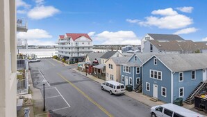 A street view with a white van parked on the side, a blue building with a red roof, and a white building with a red roof. - Unique, festive 3-bedroom luxury condo with adorable coastal decor and free WiFi located downtown on the bayside and just two blocks to the beach and Boardwalk! (Ocean City)