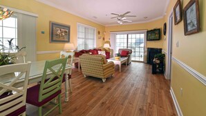 A living room with a glass dining table, green chairs, a patterned armchair, a red sofa, and a fireplace. - Unique, festive 3-bedroom luxury condo with adorable coastal decor and free WiFi located downtown on the bayside and just two blocks to the beach and Boardwalk! (Ocean City)