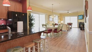 A spacious kitchen with wooden cabinets, a black refrigerator, and a dining area with a table and chairs. - Unique, festive 3-bedroom luxury condo with adorable coastal decor and free WiFi located downtown on the bayside and just two blocks to the beach and Boardwalk! (Ocean City)