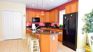 A kitchen with wooden cabinets, a black refrigerator, a microwave, and a bar stool. - Unique, festive 3-bedroom luxury condo with adorable coastal decor and free WiFi located downtown on the bayside and just two blocks to the beach and Boardwalk! (Ocean City)