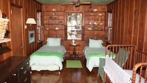 Una habitación de madera con dos camas, un tocador, una lámpara y una ventana con vistas.