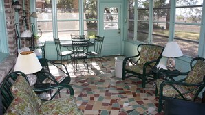 Un solárium con piso de baldosas, ventilador de techo, una mesa con sillas y una puerta que da al exterior.
