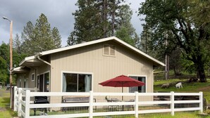 A small, single-story building with a white exterior, a red umbrella, and a white fence in front. - Family Friendly Farm Stay Near Yosemite (Mariposa)
