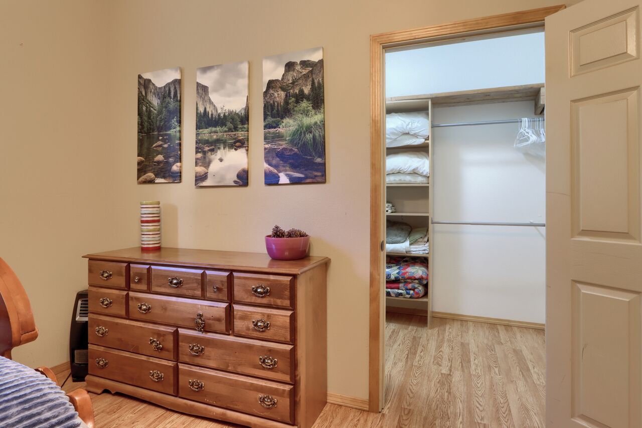 A bedroom with a wooden dresser, a bed, and a closet with hanging clothes.