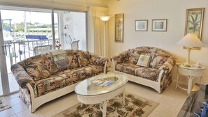 A living room with two floral-patterned sofas, a glass coffee table, a ceiling fan, and a view of the outdoors through a sliding glass door.