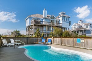 A pool area with lounge chairs and a wooden fence. - Vacation Station: Dog-friendly, Private Heated pool, Hot Tub, Foosball table (Nags Head)