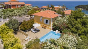 Eine mediterrane Villa mit Swimmingpool, umgeben von üppiger Vegetation und Blick auf das Meer.