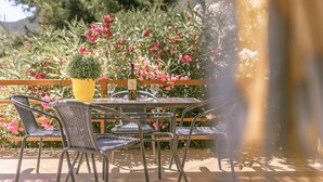 Eine Terrasse im Freien mit Tisch und Stühlen, umgeben von üppiger Vegetation und rosa Blüten.