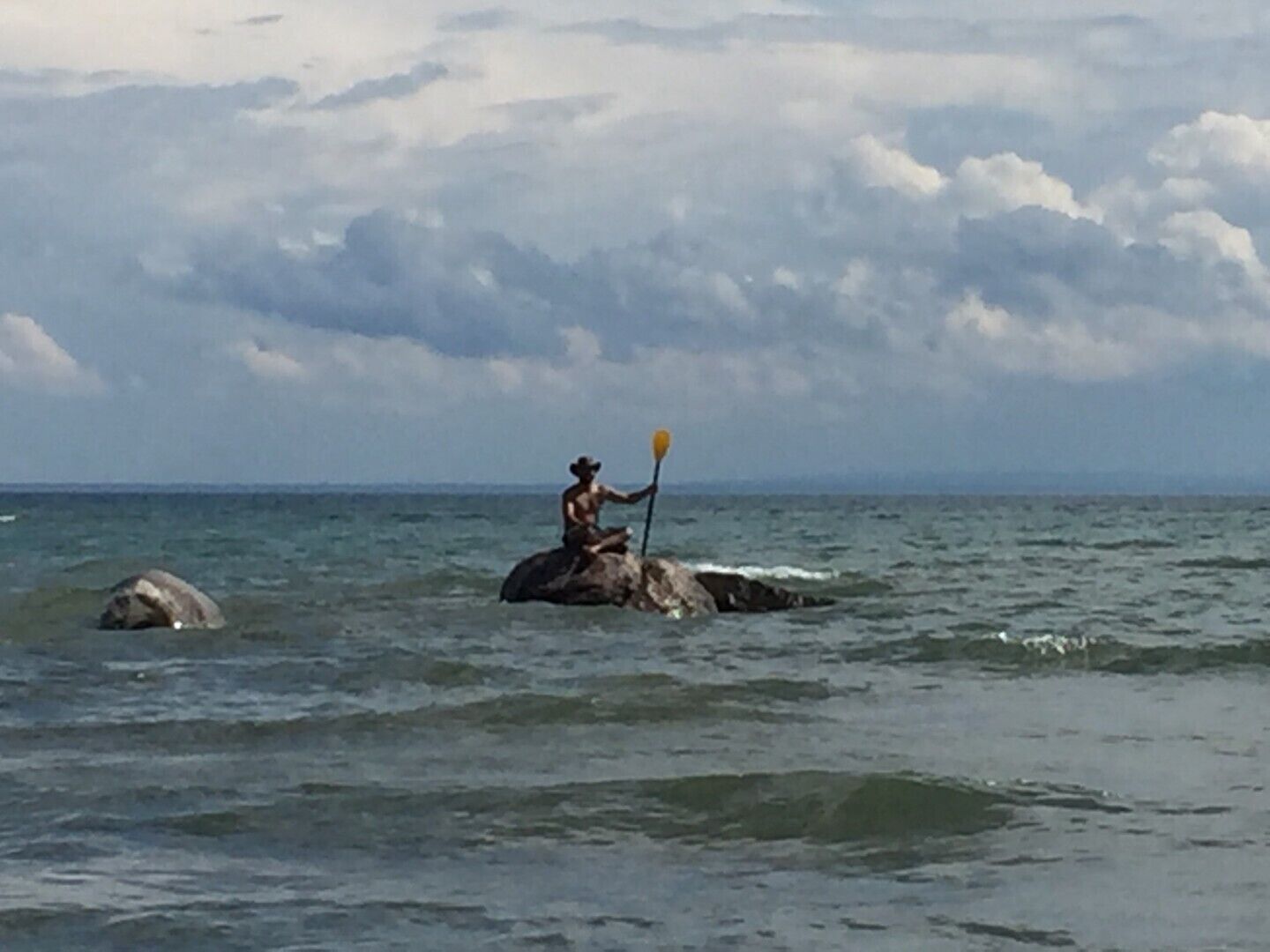 Eine Person sitzt auf einem Felsen im Meer und hält ein Paddel.