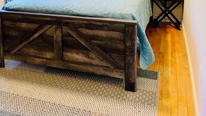 Een slaapkamer met een houten bedframe, een blauw beddegoed, twee bedlampen en een lijst met een afbeelding aan de muur.