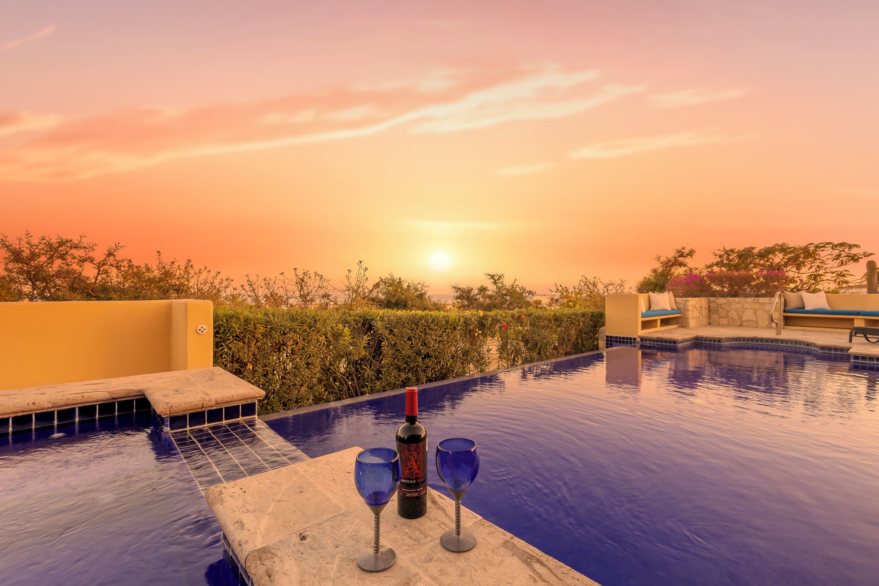 A poolside area with a sunset view, a bottle of wine, and two wine glasses.