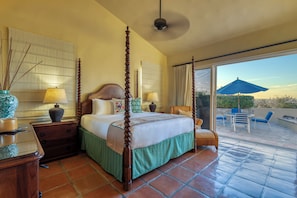 A hotel room with a four-poster bed, a balcony with outdoor seating, and a view of the landscape.