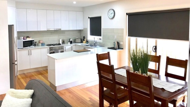 Una cocina moderna con armarios blancos, una isla central y un comedor con sillas y una mesa de madera.