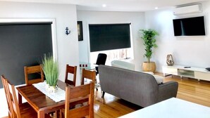Una sala de estar moderna con comedor, muebles de madera, un sofá gris, un televisor y una planta en maceta.