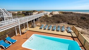 Ein Poolbereich mit Holzterrasse, Liegestühlen und Blick auf den Strand.