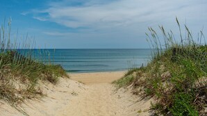 Ein Sandweg am Strand, der zum Meer führt, umgeben von Gras und Dünen.