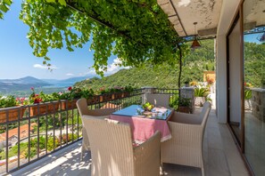 A balcony with wicker furniture, a table with a red and white checkered tablecloth, and potted plants.