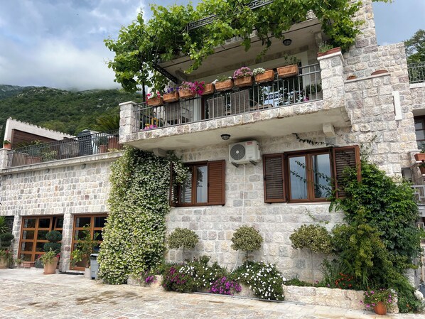 A stone building with a balcony, potted plants, and a view of the surrounding landscape.