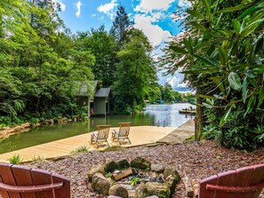 Une terrasse au bord de la rivière, avec des chaises en bois, un foyer et un petit abri de jardin.