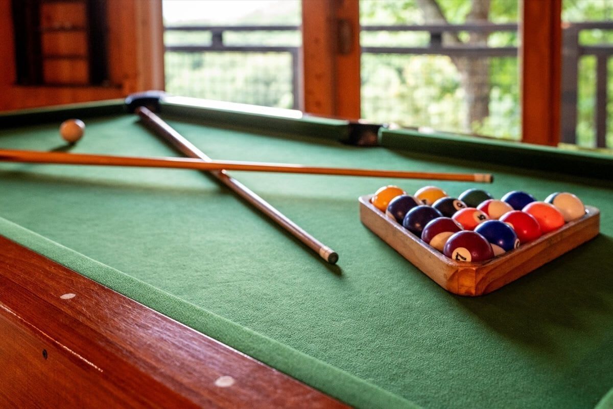 A pool table with a cue stick and a rack of billiard balls.