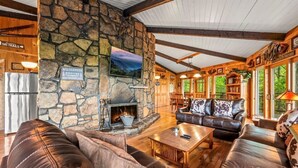 A cozy lodge interior with stone walls, leather furniture, a fireplace, and a view of the outdoors.