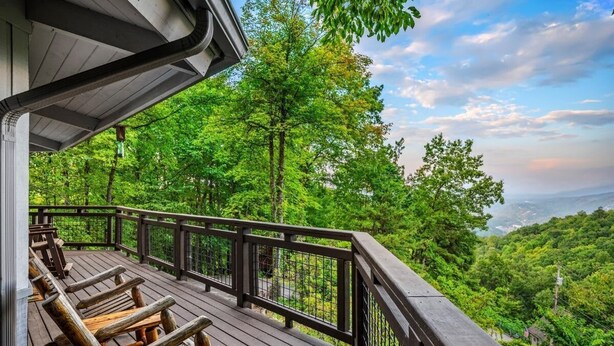 A wooden deck with benches, a railing, and a view of a forested landscape.