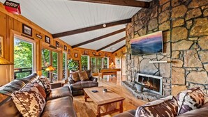 A cozy living room with leather sofas, a fireplace, stone walls, and framed pictures on the walls.