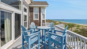 A balcony with blue Adirondack chairs and a table overlooking a beach and ocean. - Beach Breeze: Oceanfront, Pool, Hot Tub, Elevator (Nags Head)