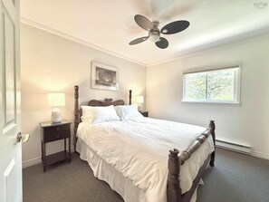 A bedroom with a bed, two bedside tables, a ceiling fan, a window, and a door. - OCEAN SURF COTTAGE AT SUMMERVILLE BEACH (Summerville Centre)