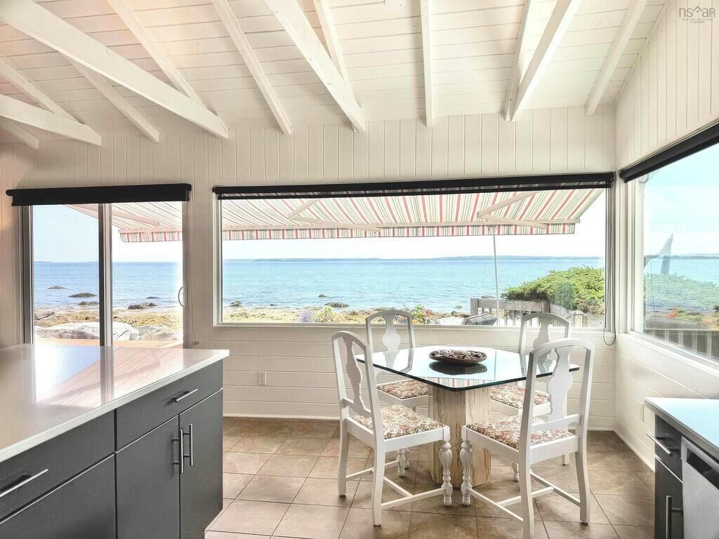 A kitchen with a view of the sea, a dining table with chairs, and a large window.