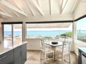 A kitchen with a view of the sea, a dining table with chairs, and a large window.