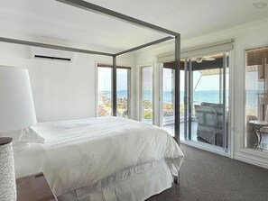 A bedroom with a large bed, a view of the sea, and a balcony with a table and chairs.