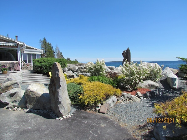 Una propiedad costera con una escultura de piedra, un patio con mobiliario exterior y vistas al mar.