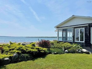 Una propiedad costera con una sala con paredes de vidrio, un césped y vista al mar.