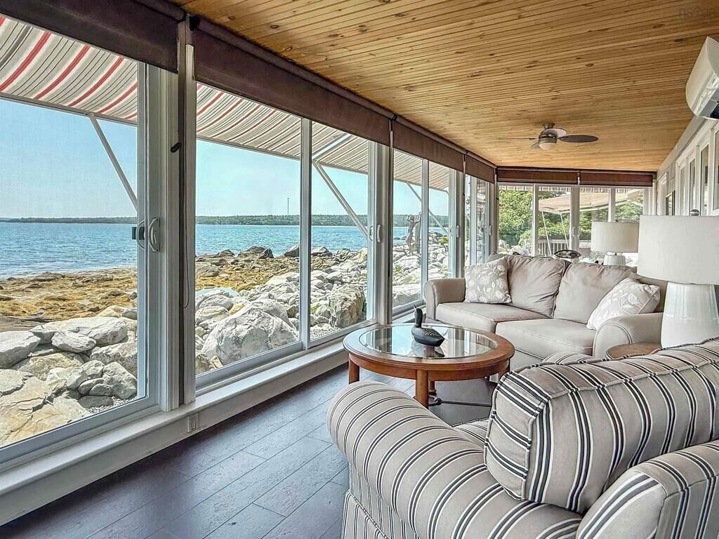 Une pièce dotée d’une grande fenêtre donnant sur une côte rocheuse, d’un canapé, d’une table basse et d’un ventilateur de plafond.