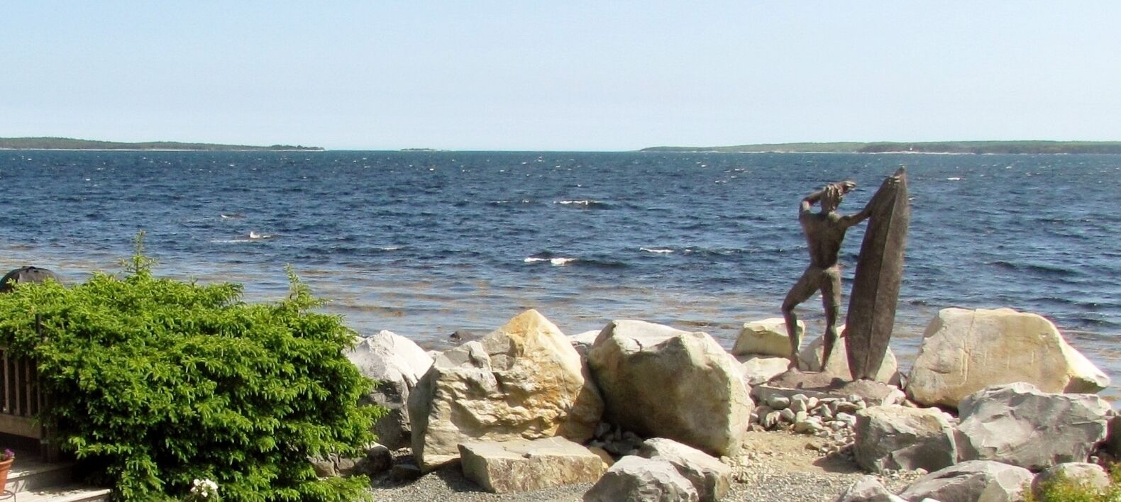 Une côte rocheuse avec une statue représentant deux personnages, une étendue d’eau et une terre lointaine.
