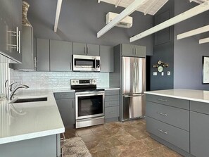 A modern kitchen with grey cabinetry, stainless steel appliances, and a tiled backsplash.