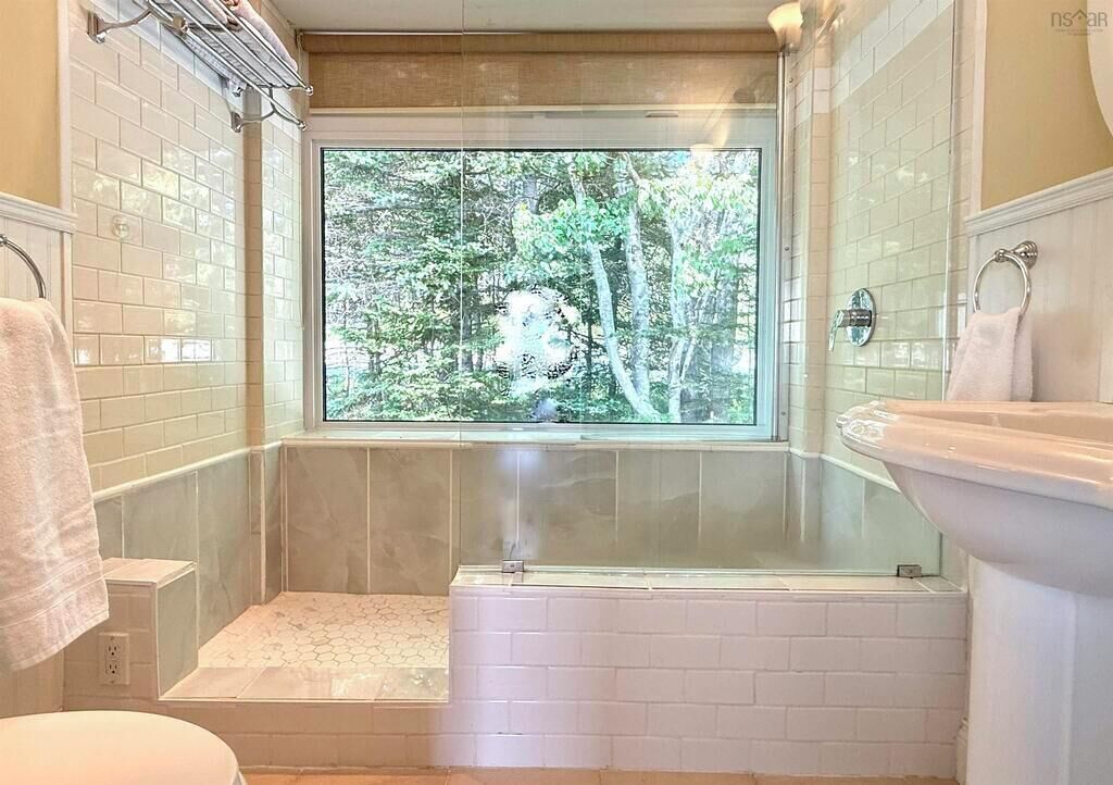 Une salle de bain avec une baignoire, une fenêtre donnant sur la forêt et des toilettes.