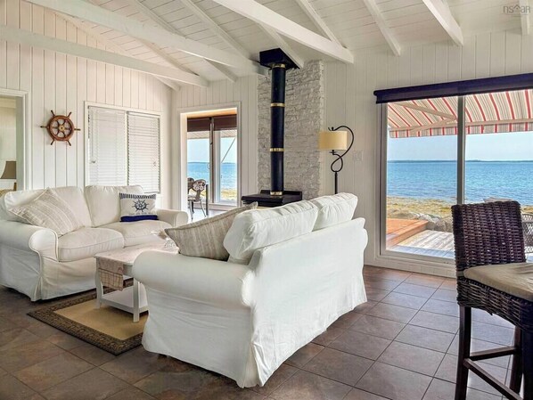 A coastal living room with a white sofa, a wicker chair, and a view of the sea.