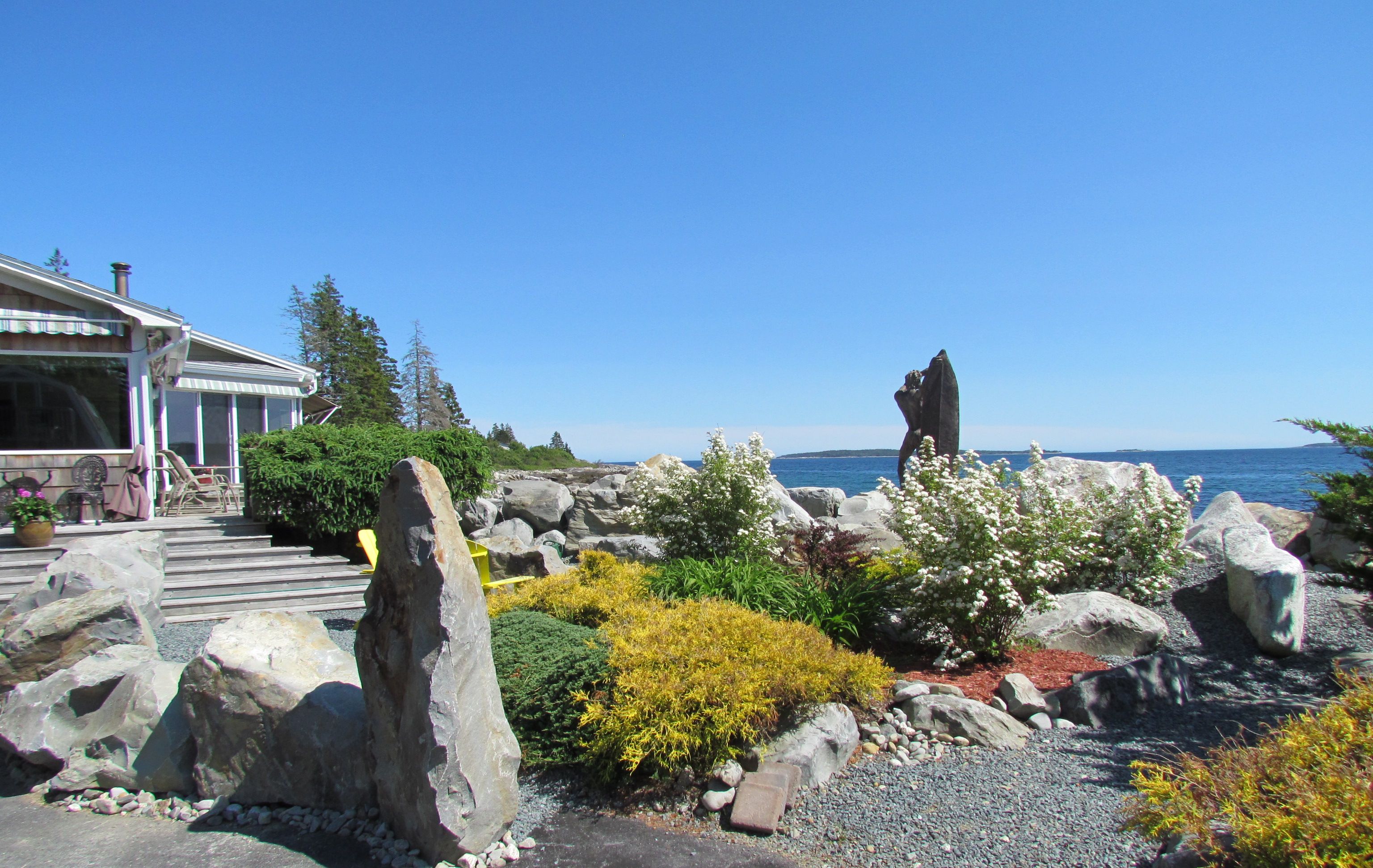 Une propriété située sur la côte, agrémentée d’une sculpture en pierre, d’une terrasse avec mobilier d’extérieur et offrant une vue sur la mer.