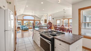 Una cocina amplia con una isla central, un comedor con sillas rojas y ventanas grandes que ofrecen vistas al exterior.