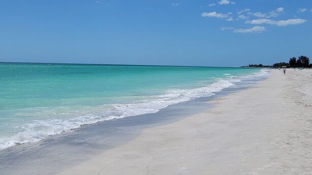 Une plage aux eaux turquoise et limpides, bordée d’un rivage sablonneux.