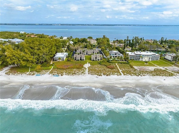 An aerial view of a coastal resort with multiple buildings, a beachfront, and a view of the ocean.