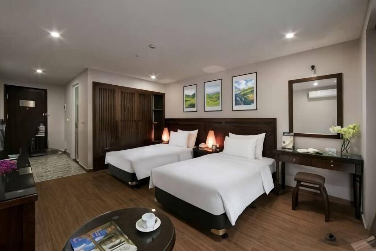 A hotel room with two beds, a desk, a chair, a coffee table, and a mirror.