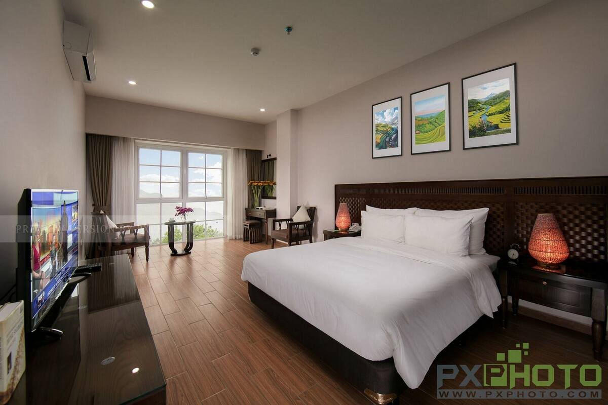 A hotel room with a large bed, a desk with a computer, a TV, and a window with curtains.